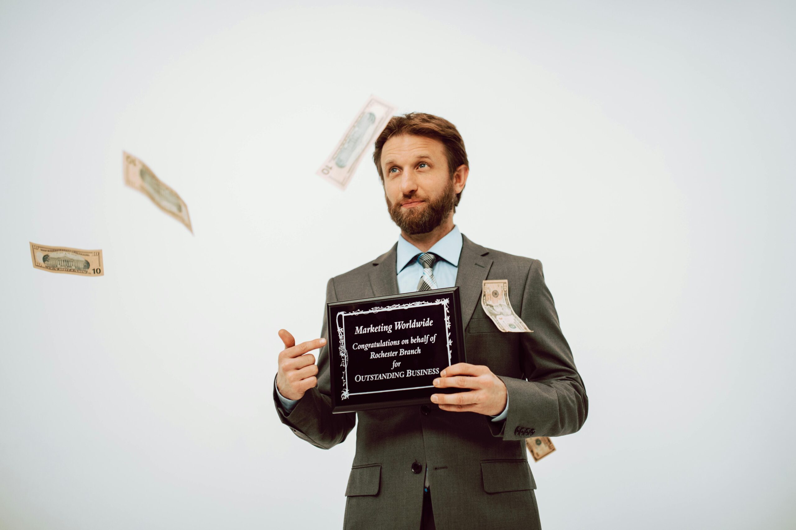 Businessman holding an award plaque, surrounded by falling cash, symbolizing success.